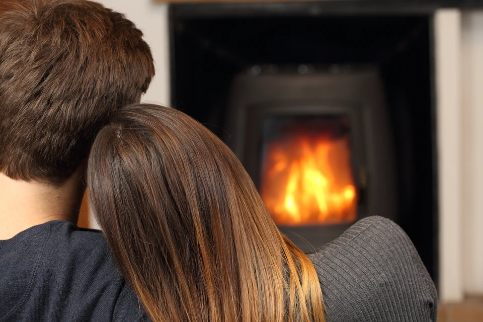 Couple assis côte à côte devant une cheminée allumée dans un salon cosy, vue de dos, atmosphère intime et chaleureuse