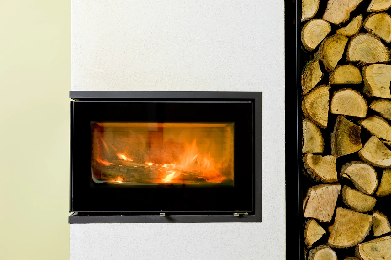 Intérieur moderne avec cheminée à foyer fermé en fonctionnement, flammes oranges visibles à travers la vitre