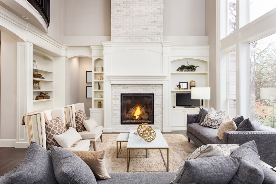 Salon moderne avec cheminée centrale allumée, mobilier gris et beige disposé symétriquement