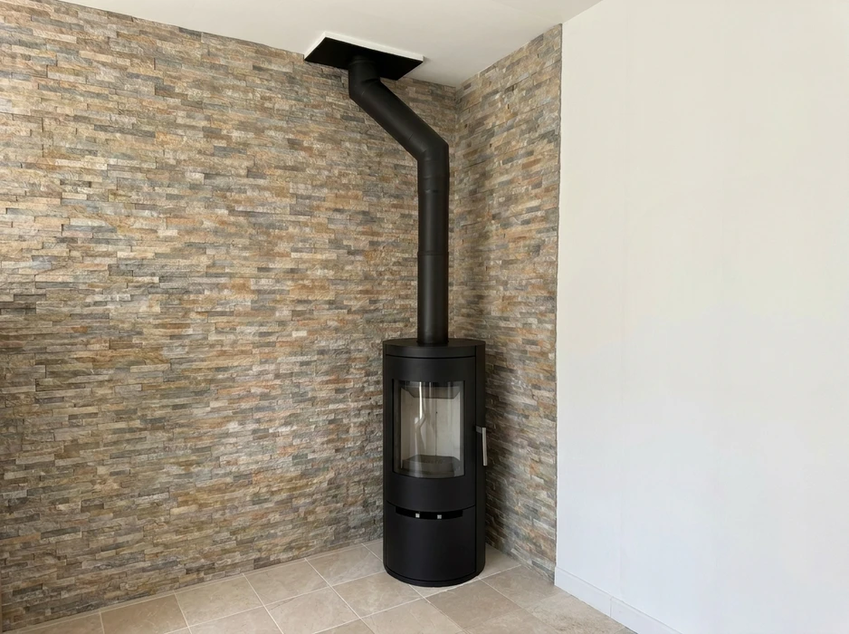 Poêle à bois design cylindrique noir mat installé en angle, raccordé par un conduit de fumée noir coudé