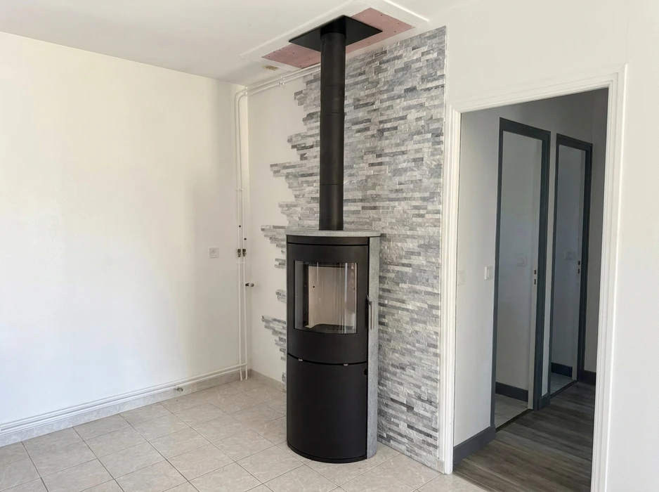 Pièce intérieure vide avec poêle à bois design noir cylindrique de type scandinave, vitré frontal, sur socle, avec conduit de fumée apparent