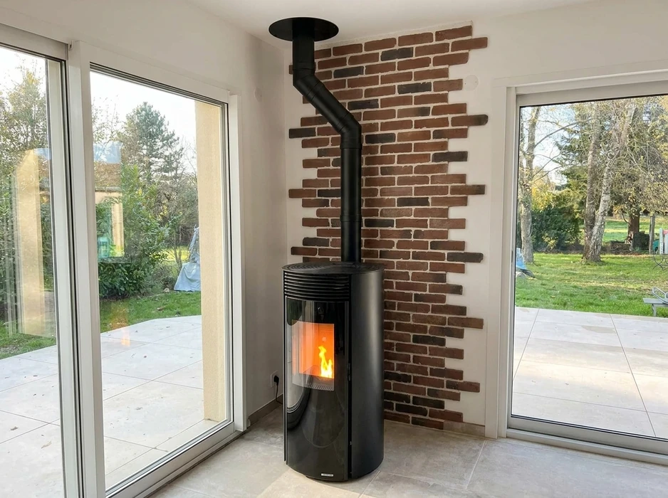 Poêle à granulés cylindrique noir brillant, installé dans un espace de vie lumineux avec baies vitrées donnant sur jardin